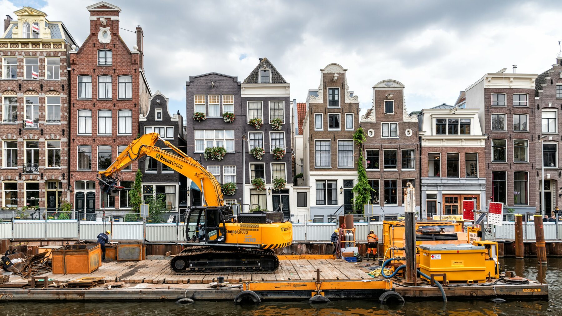 Machines voor kadevernieuwing op een ponton aan een typische Amsterdamse gracht.