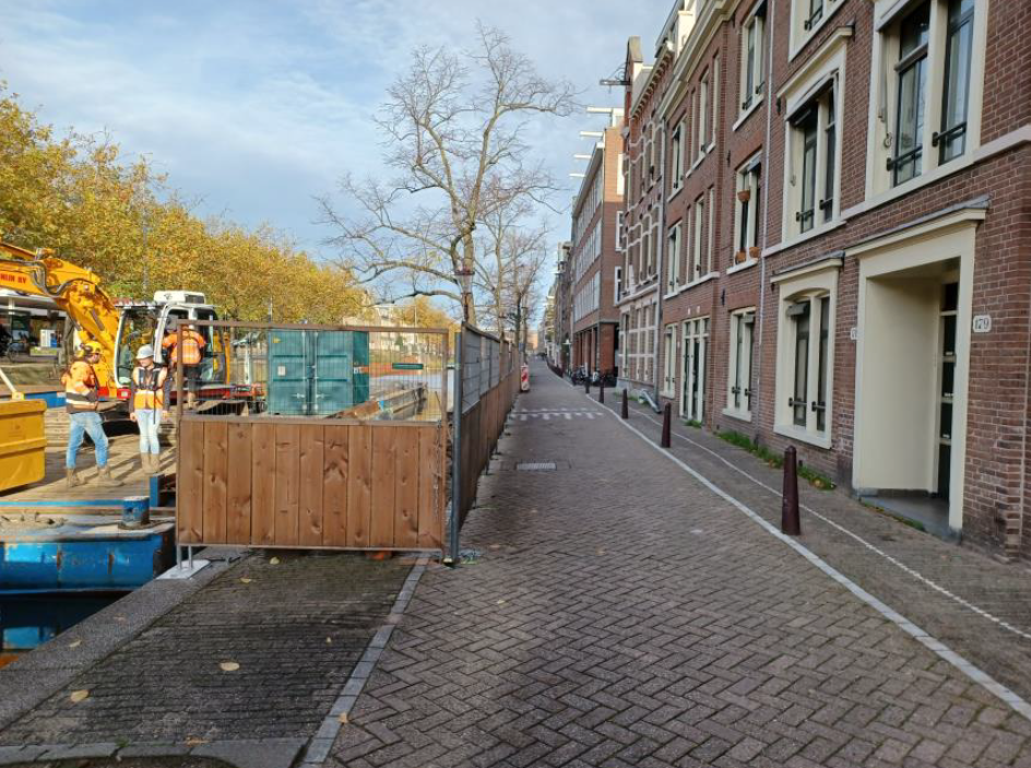 Zicht op rijweg Lijnbaansgracht met links vanaf de parkeervakken het bouwterrein van Kade 2.020 met werklui en een kraan op het ponton