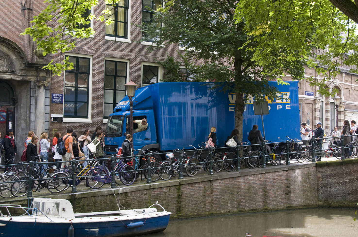 Een vrachtwagen op een gracht in de binnenstad maakt een nauwe bocht de brug af tussen fietsers en voetgangers