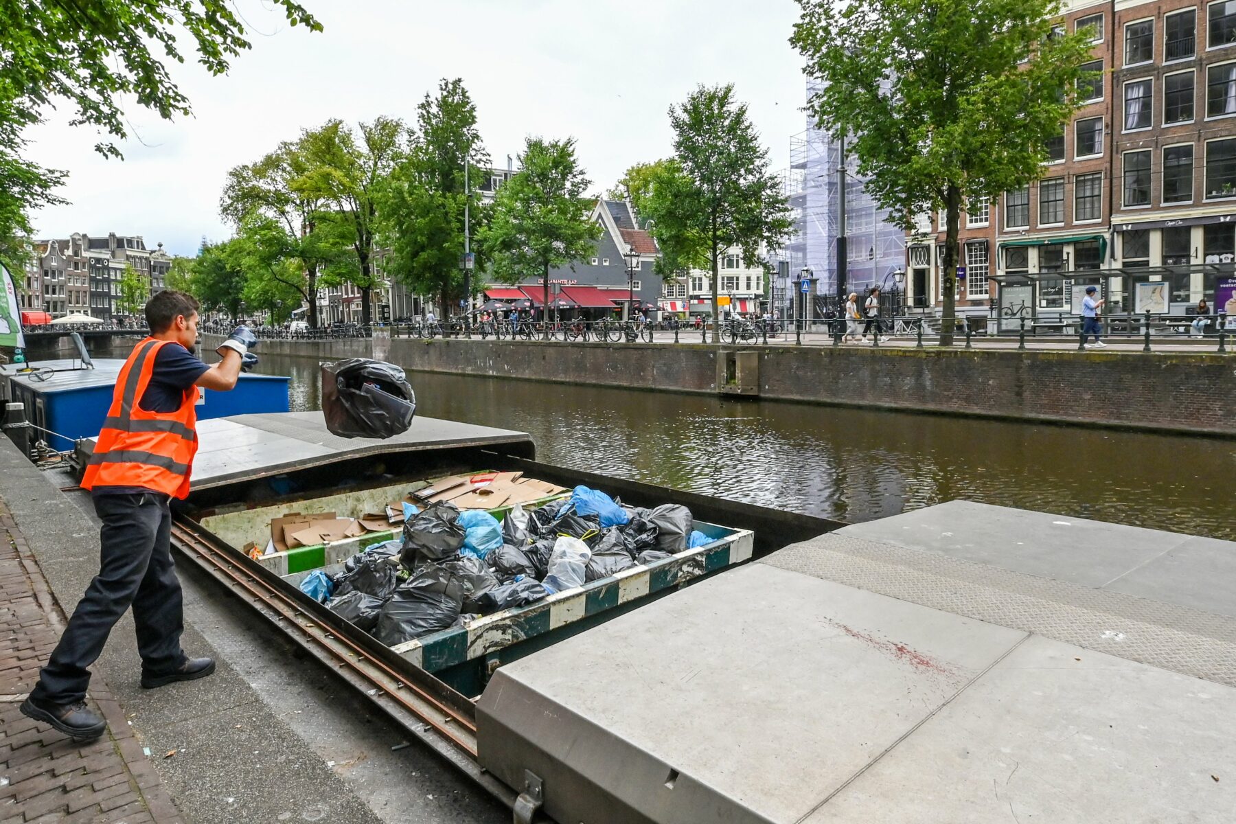 Vuilnisman gooit een zak in een afvalboot op de gracht. Dit gaat over een proef met kleinschalig ophalen afval dat per boot naar vuilverbranding gaat