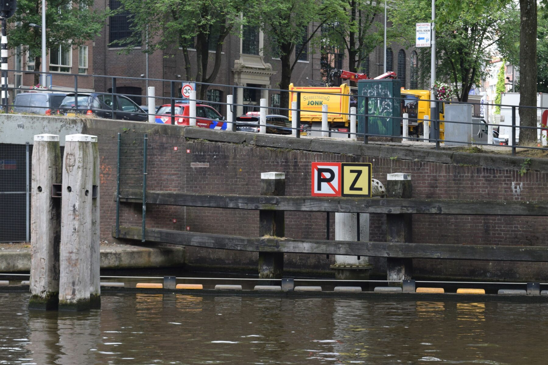 Kademuur met bord Zinker en bord Niet aanleggen. Achter de borden een rioolbuis die vanaf de kant de gracht in gaat.