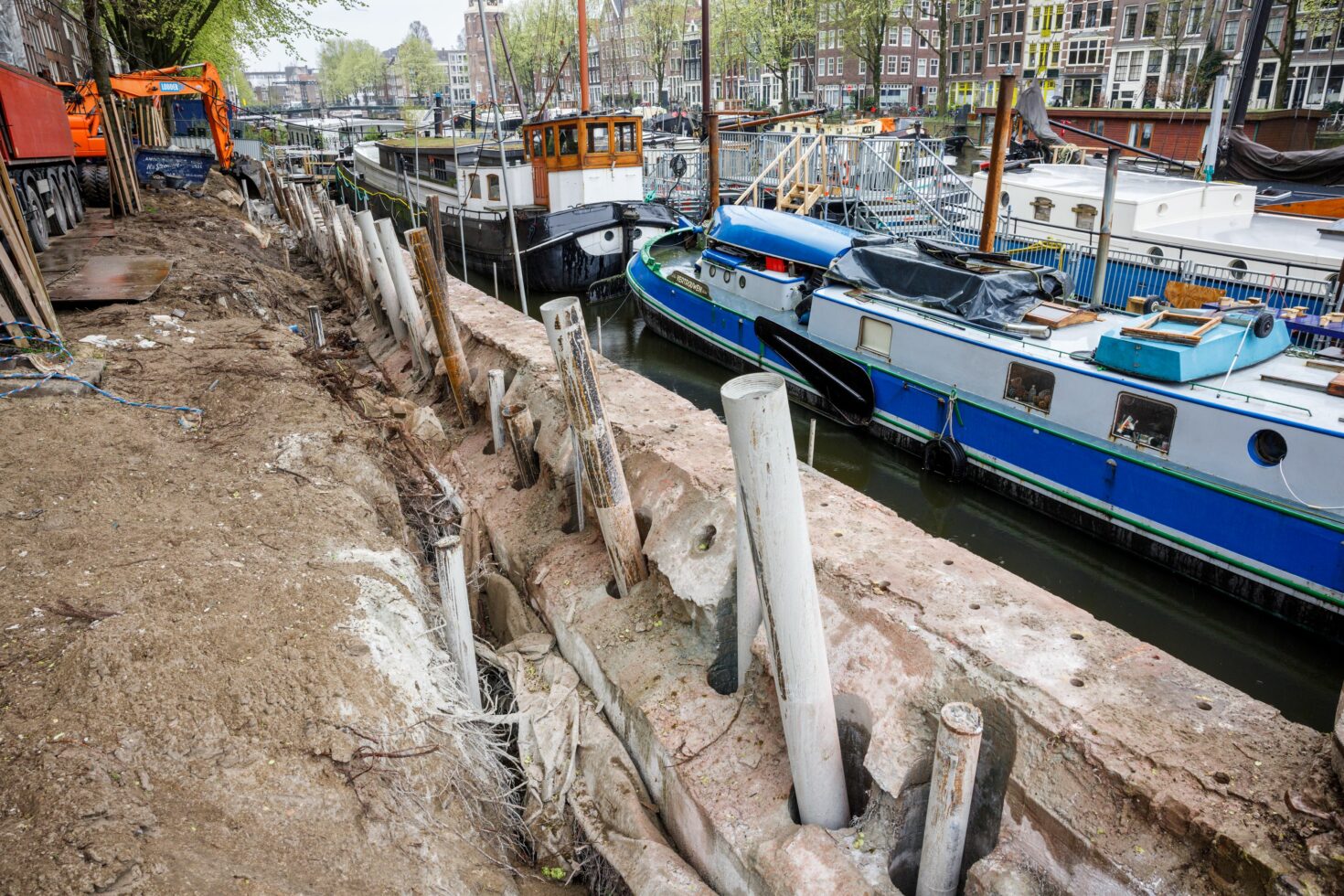 De oude kademuur met daardoorheen geboord een rij groutinjectiepalen die om en om recht en schuin (schoor) staan