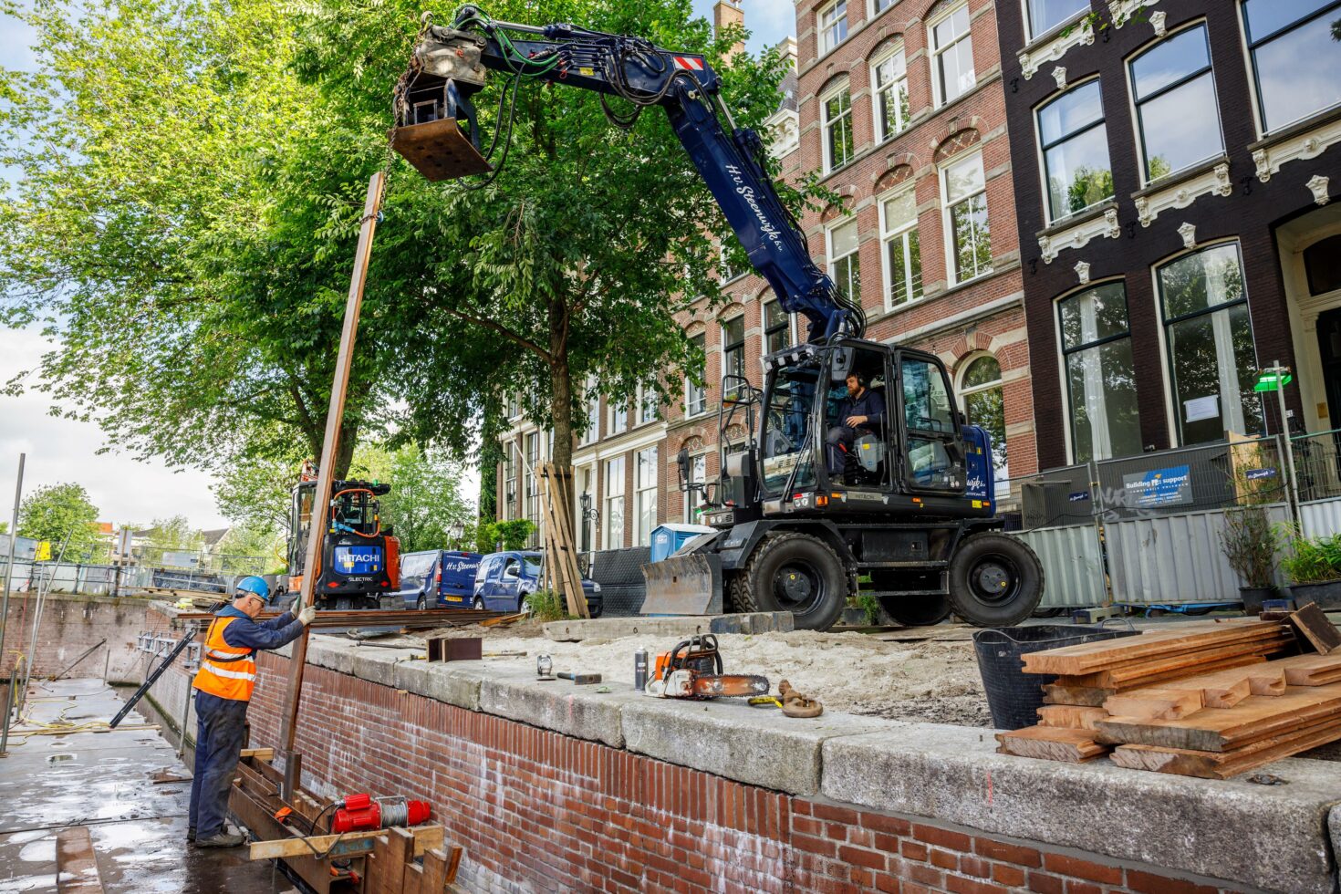 Een kraanwagen reikt een lange plank aan voor de bouw van het onderloopheidsscherm