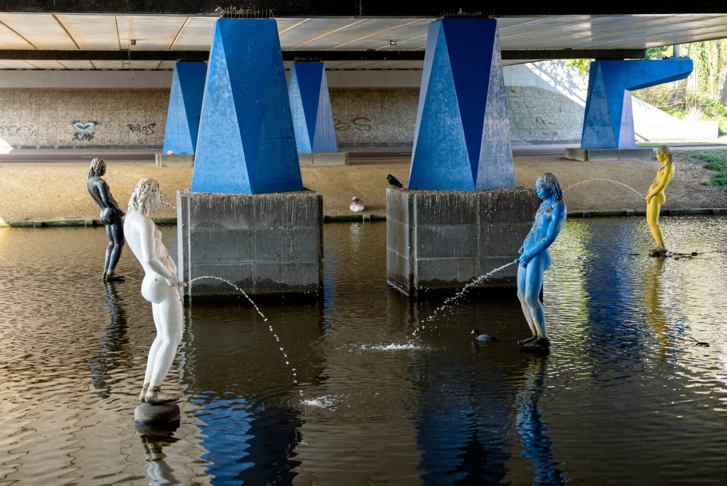 Vier van de zes plassende beelden in het water onder de Groesbeekdreef, die samen het kunstwerk Les Pisseurs d'Amsterdam vormen