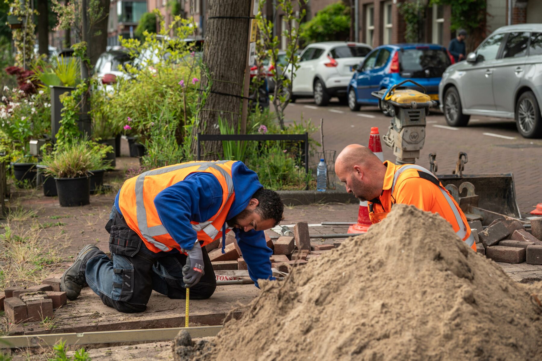 Miguel en René aan het werk op de kade met voor hen een hoop zand die ze hebben uitgegraven. Miguel meet de diepte van het gat tot de kadevloer