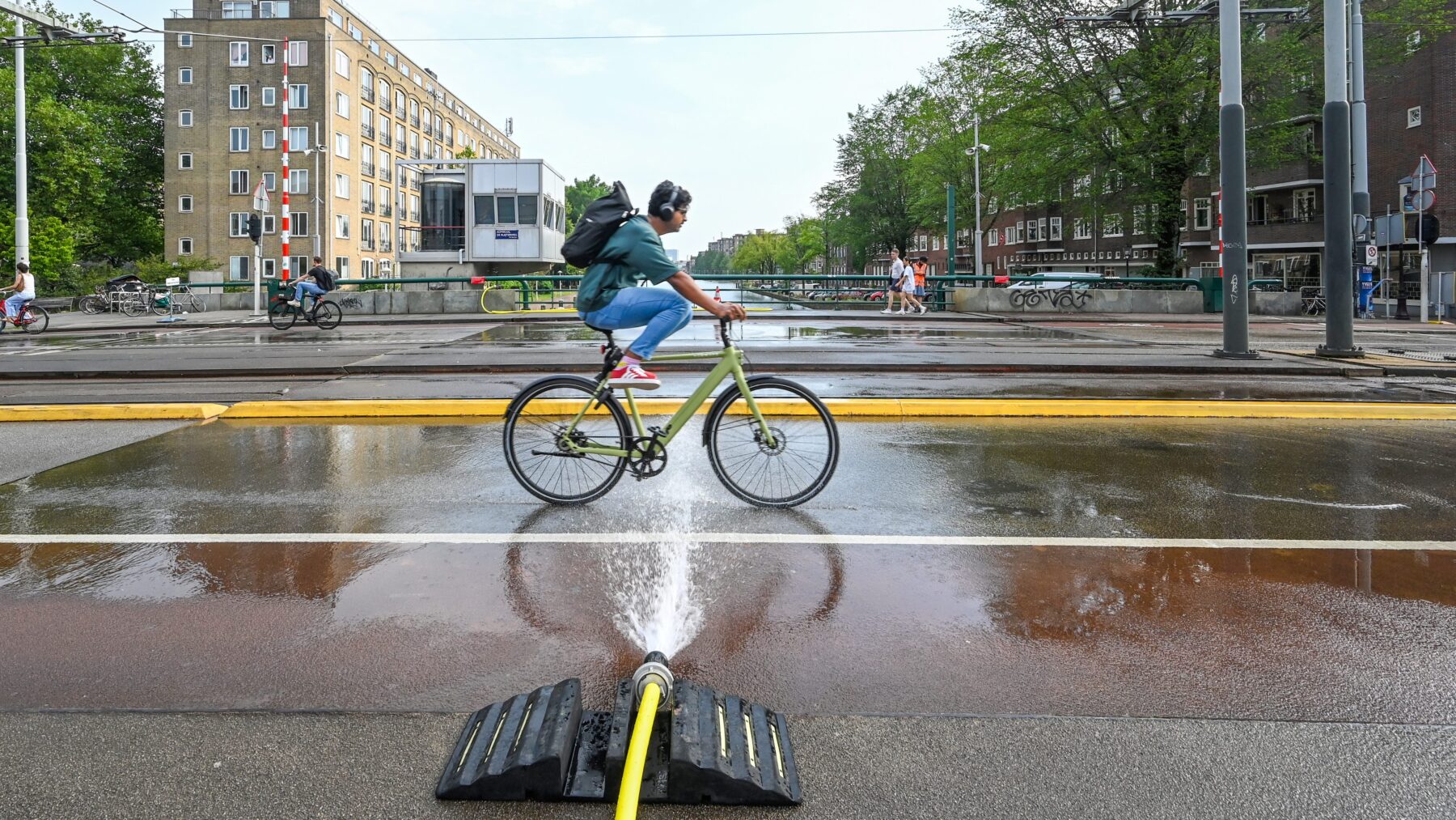 Fietser met koptelefoon tilt zijn benen op om het bluswater te ontwijken op de Wiegbrug