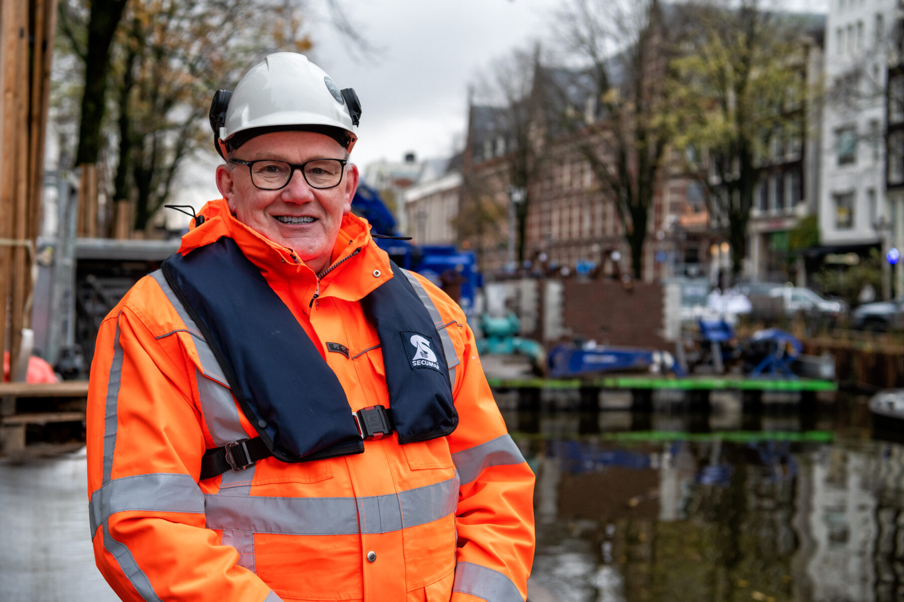 Een portretfoto van veiligheidskundige Ruud Buren, met een oranje werkjas aan, helm op