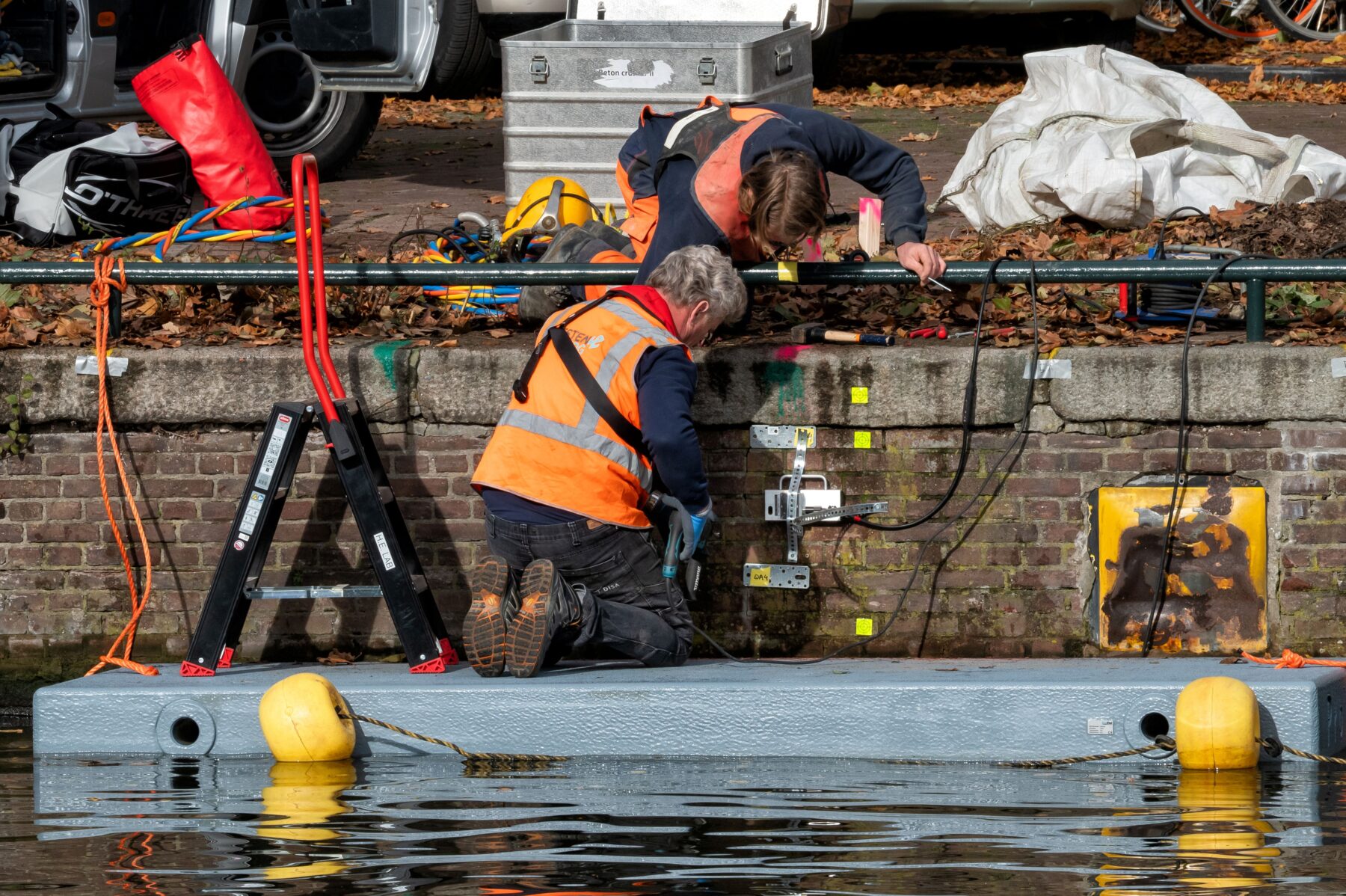 2 mannen plaatsen apparatuur op en tegen de kademuur