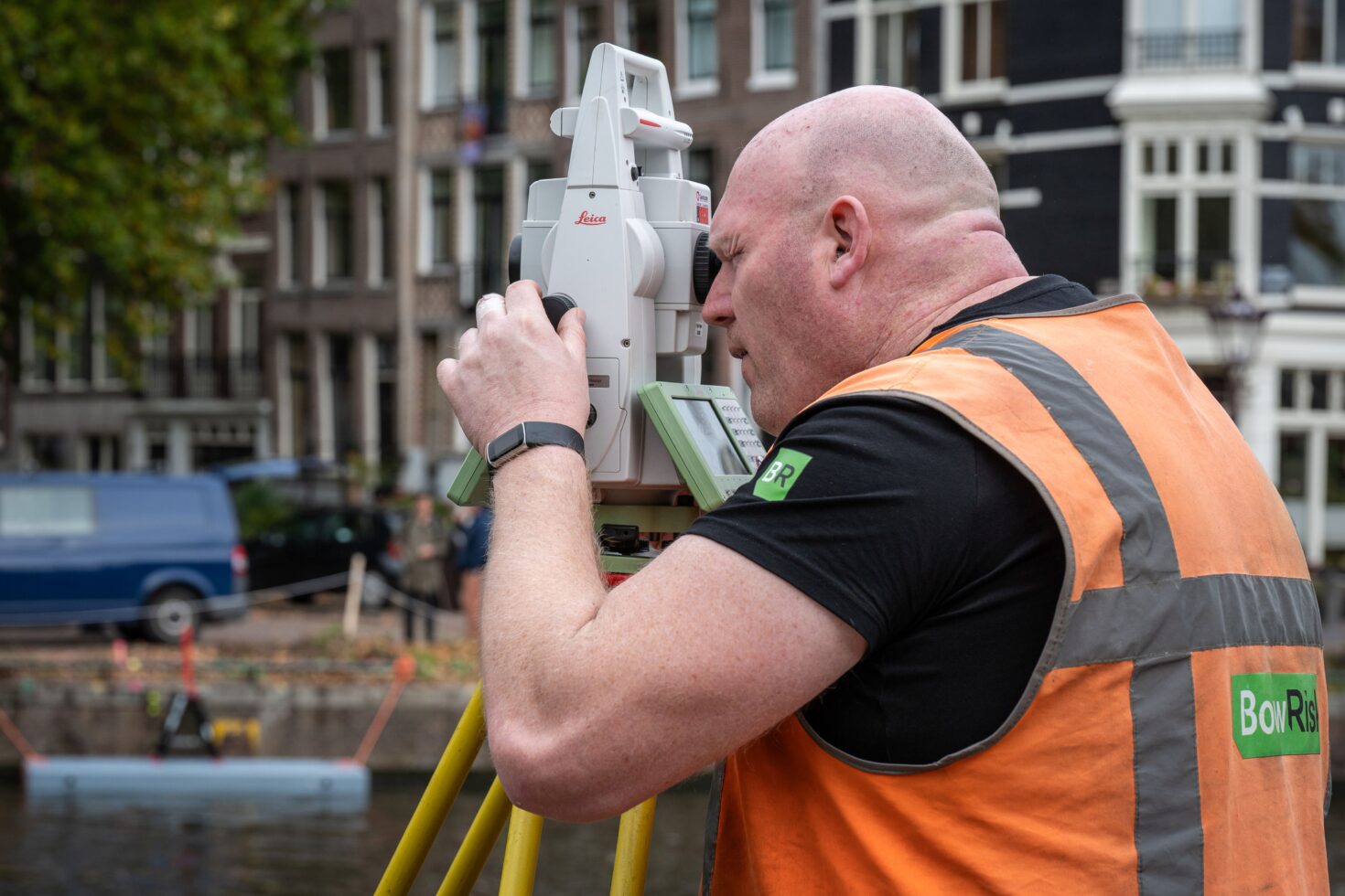 Een landmeter kijkt door het oog van een total station naar de kade