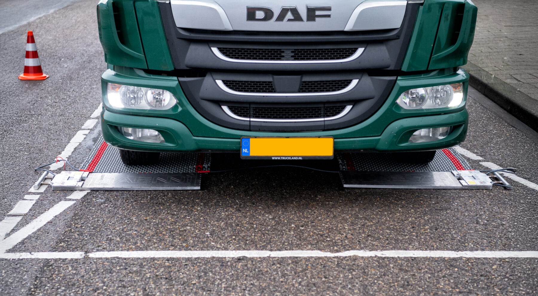 Voorkant van vrachtwagen met wielen op een aanrijdmat. De vrachtwagen wordt gewogen op de metalen weegplaten die daarvoor liggen.