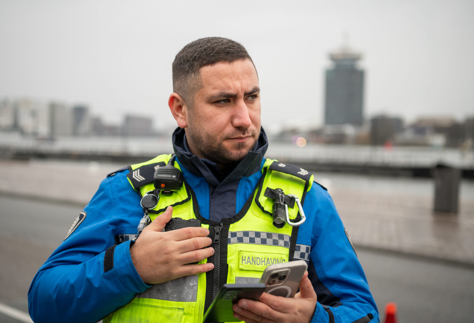 Handhaver aan het IJ met mobiele telefoon en portofoon. Op de achtergrond de A'dam Toren