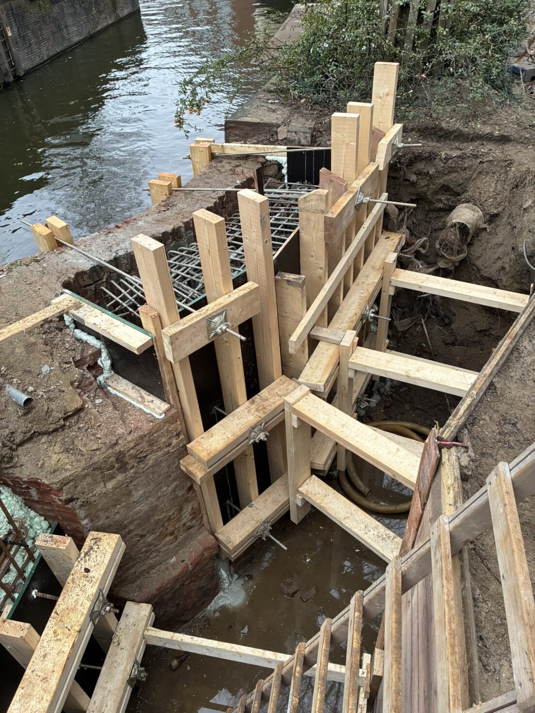 Bouwkuip achter een van de vleugelmuren met wapening en bekisting voor het beton.