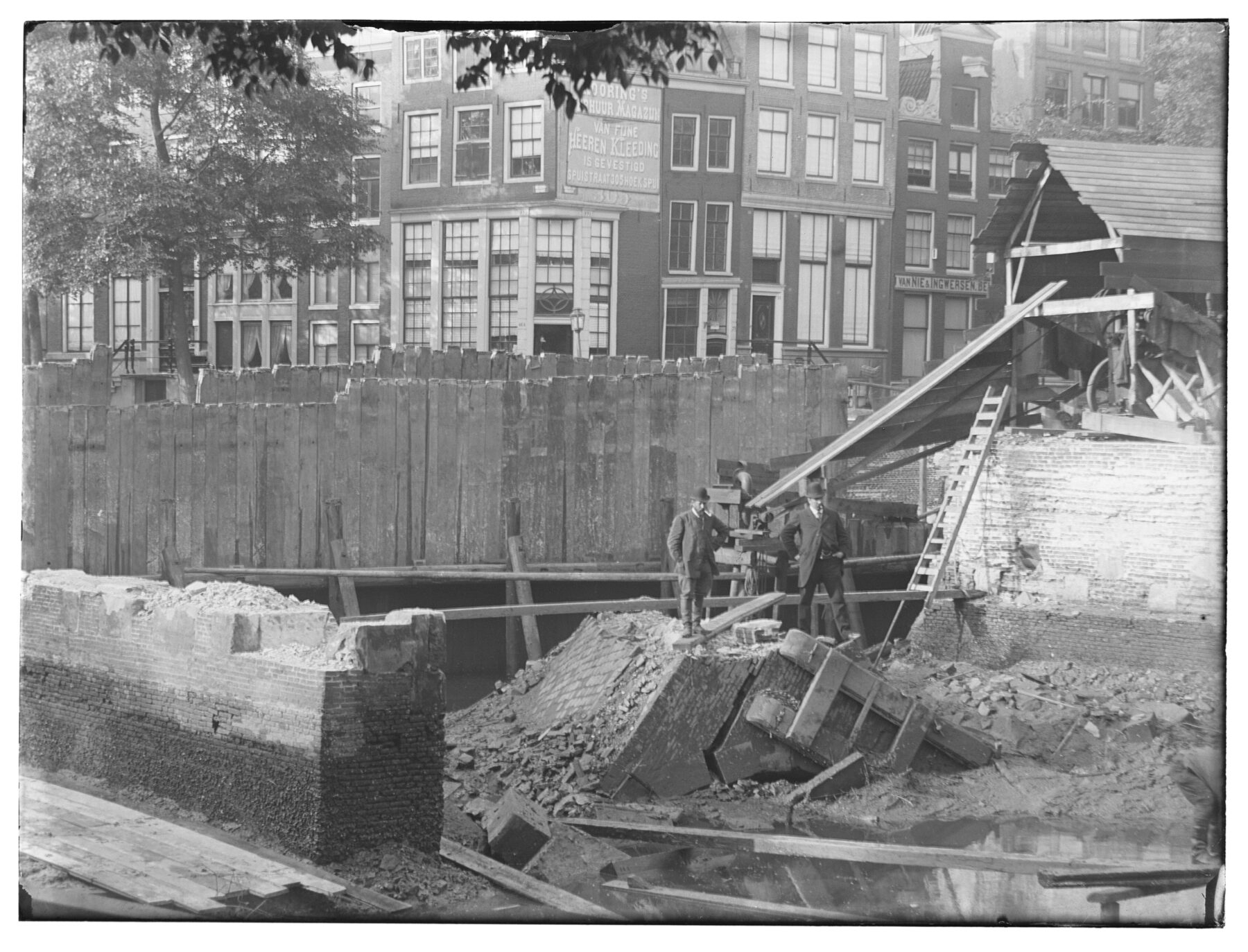 Bouwkuip voor de wederopbouw van de ingestorte brug 46. 2 heren poseren op het puin.