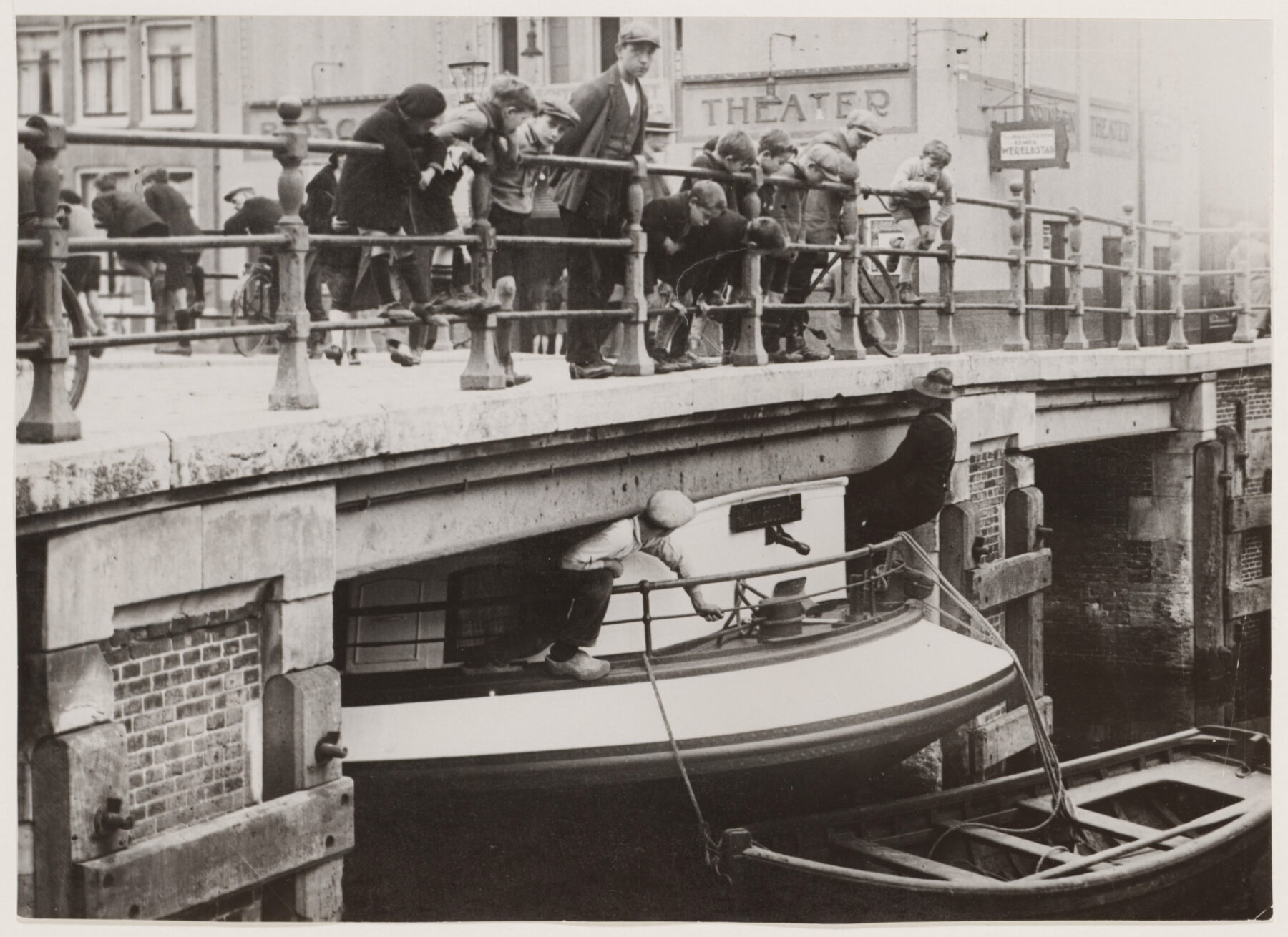 Amsterdammers kijken vanaf de brug toe hoe een schip met moeite onder de Leliesluis door wordt geloodst.