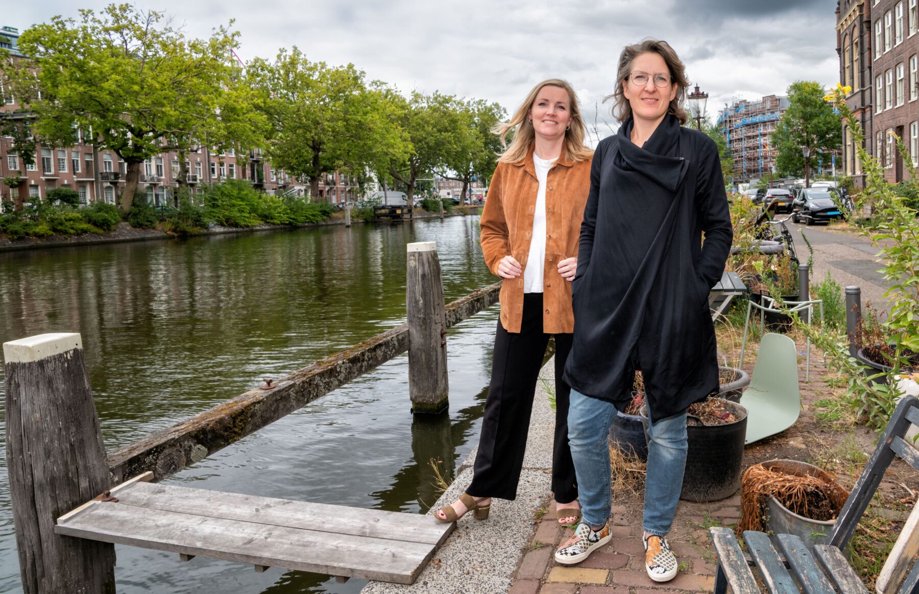 Lara Borst en Laura Hakvoort op de kade bij de Marnixkade. Rechts huizen en wat groen, links de Singelgracht met bomen en daarachter huizen aan de overkant.